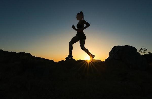 A woman running up a hill in silhouette as the sun sets.
