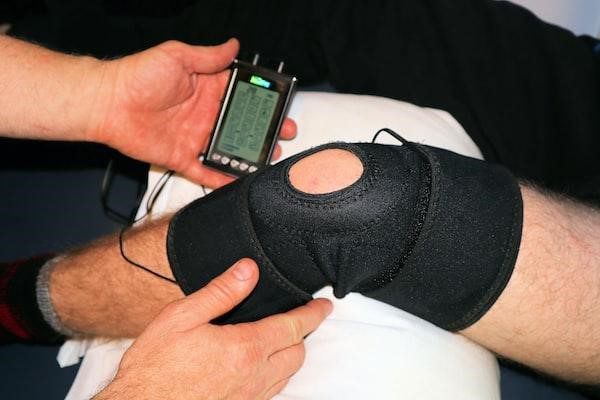 A physical therapist examines the leg of a man wearing a knee brace.